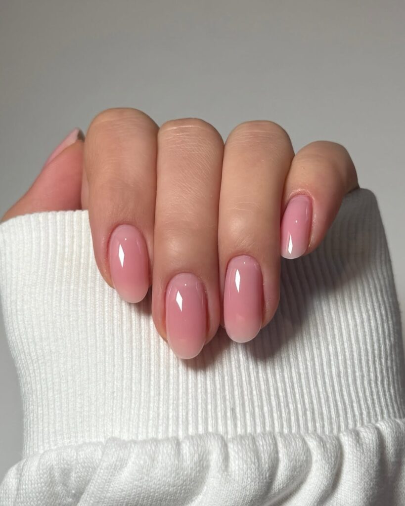 Mão de pele clara, com unha amendoada nude com fundo rosa 