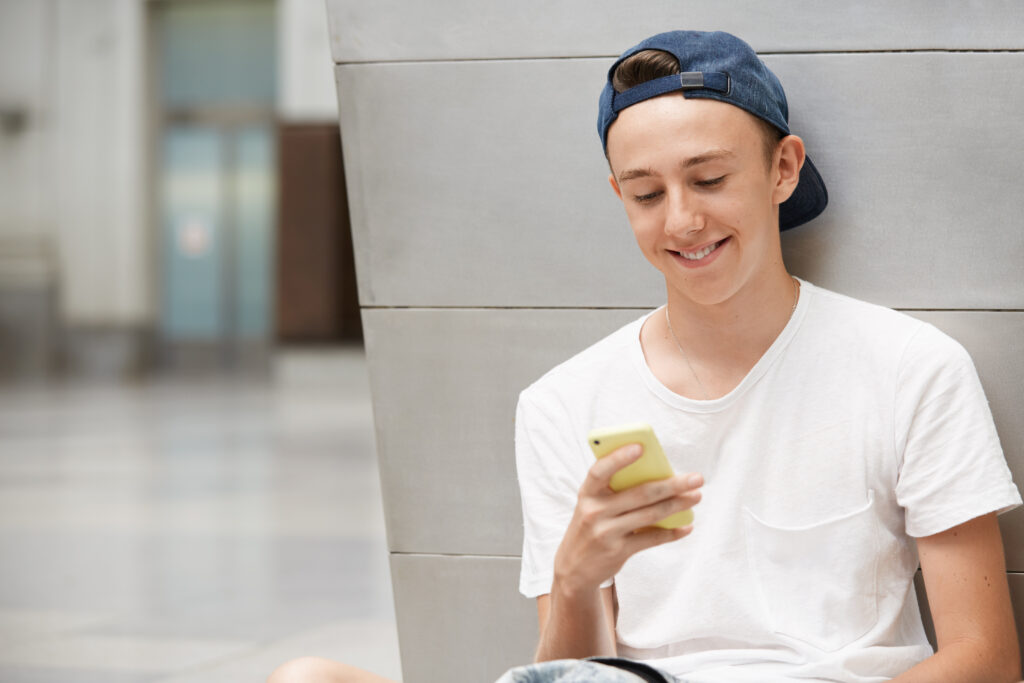 Jovem com boné e blusa branca mexendo no celular