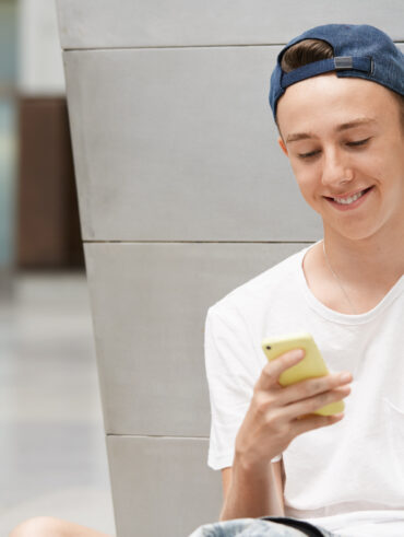 Jovem com boné e blusa branca mexendo no celular