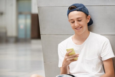 Jovem com boné e blusa branca mexendo no celular