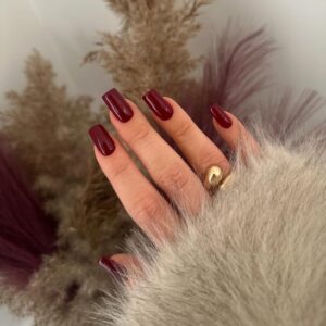 Mão de pele clara, com anel dourado e unha quadrada burgundy