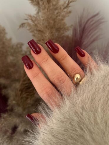 Mão de pele clara, com anel dourado e unha quadrada burgundy
