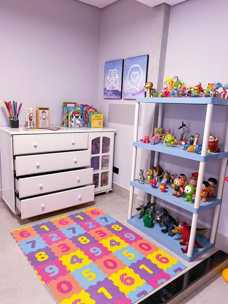 Brinquedoteca com tapete colorido com lúmeros, cômoda branca e prateleira com brinquedos