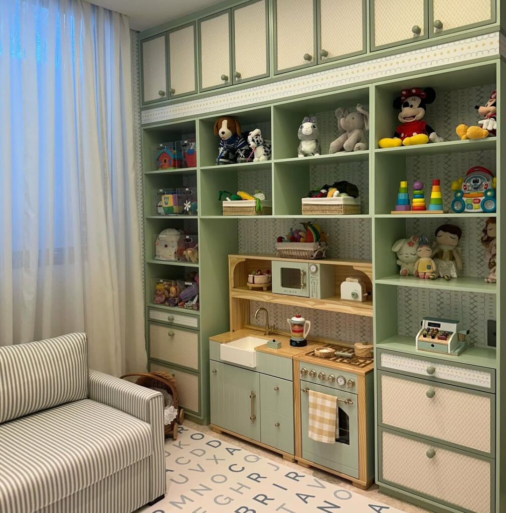 Brinquedoteca com tapete branco com letras azuis, prateleiras verdes com brinquedo