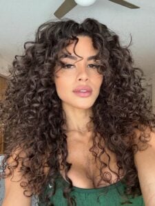 Mulher de pele clara, com blusa verde e cabelo escuro cacheado com franja