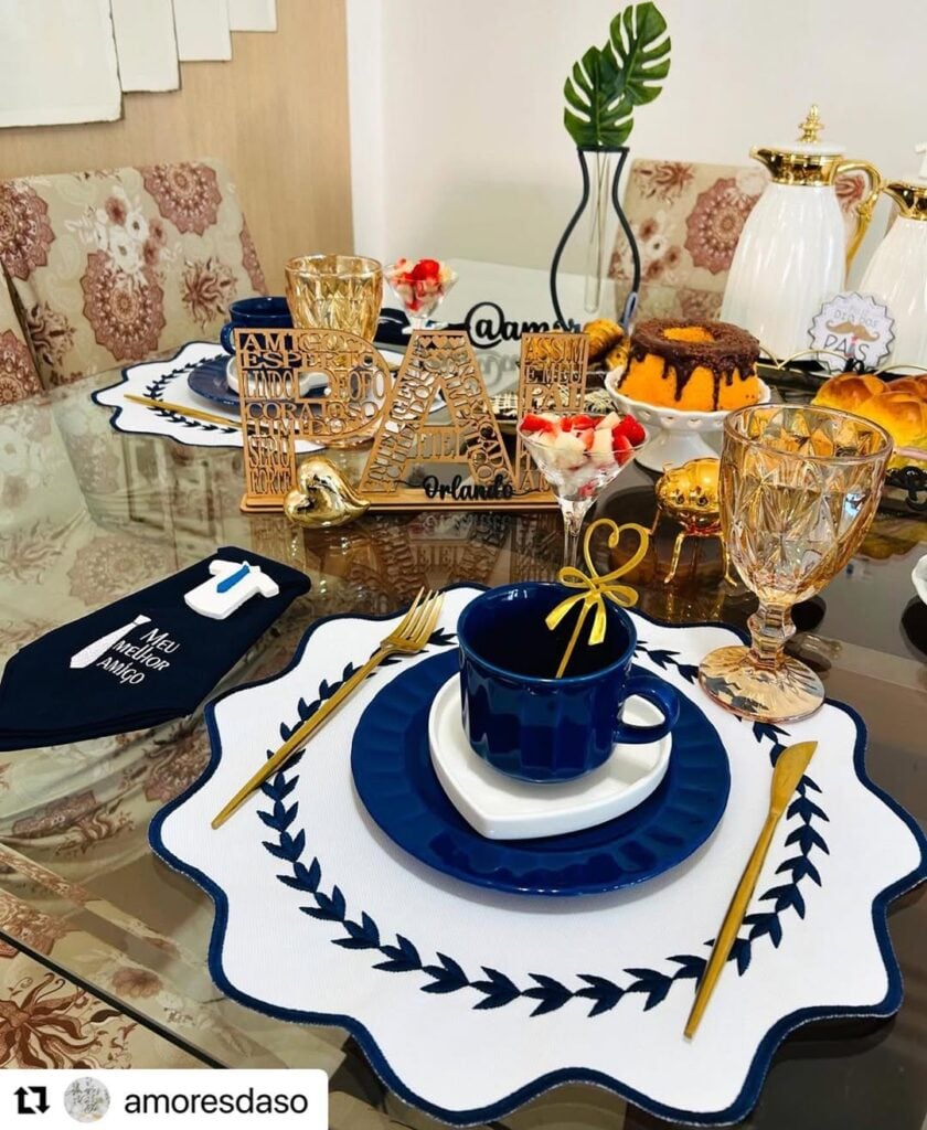 Mesa posta com sousplat branco e azul e louças azul-marinho, bolos e enfeites