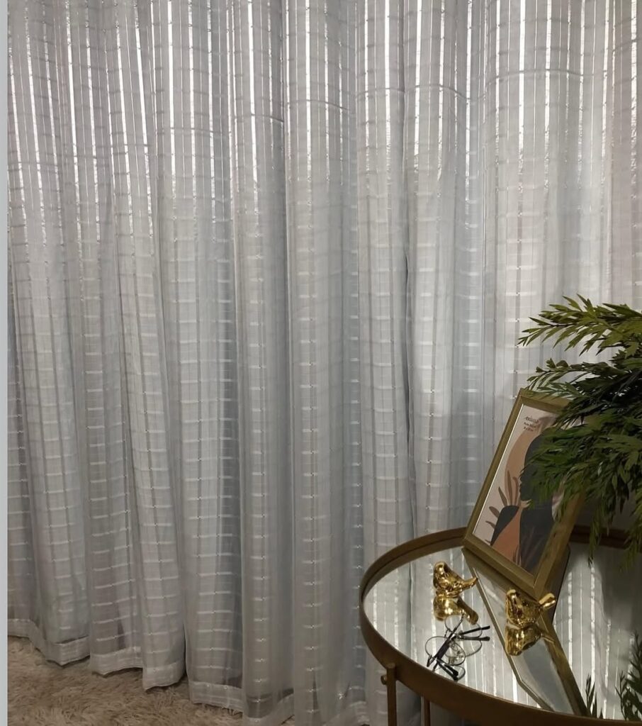 Ambiente com cortina blackout, mesa de canto com tampo espelhado e objetos decorativos