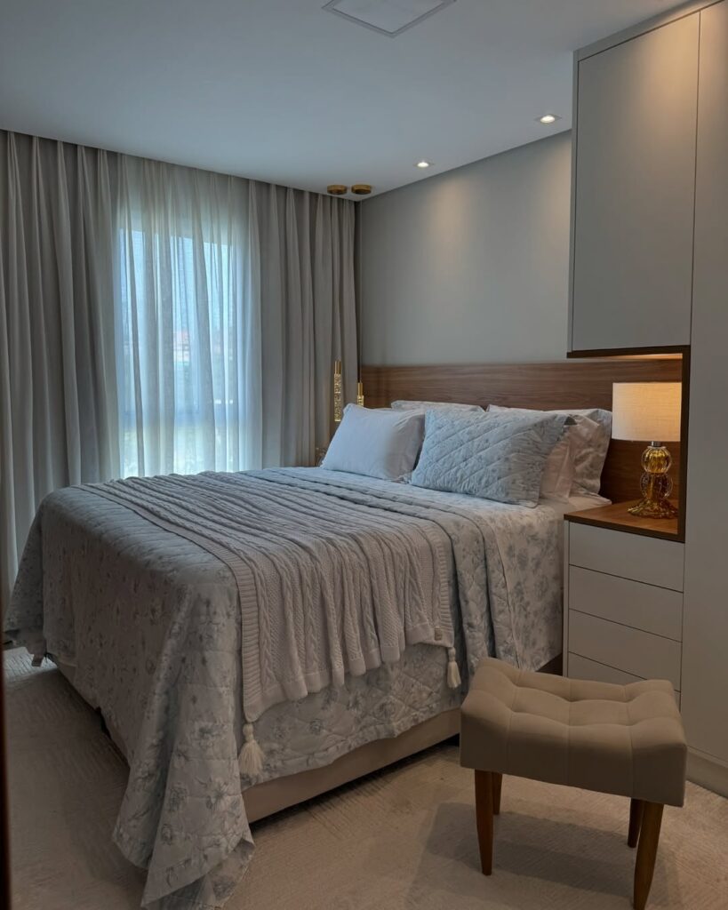 Quarto de casal com cabeceira de madeira, abajur e cortina branca