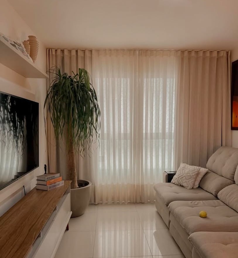 Sala de estar em tons neutros com rack, vaso com planta e cortina clara