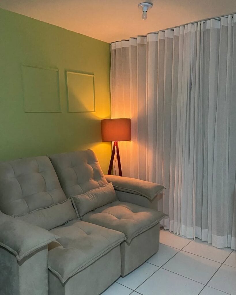Sala com sofá cinza, cortina branca e luminária de piso