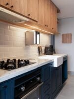 Cozinha pequena planejada com frontão de tijolinhos, armário debaixo azul e aéreo amadeirado