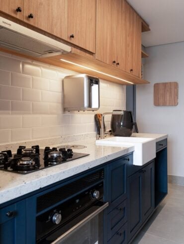 Cozinha pequena planejada com frontão de tijolinhos, armário debaixo azul e aéreo amadeirado