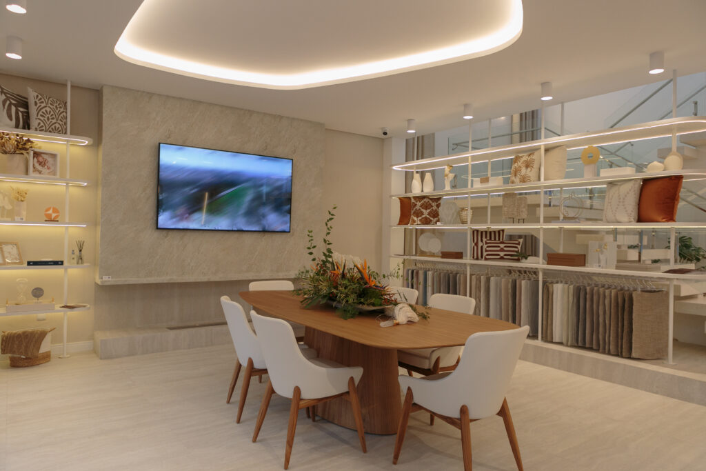 Sala de reunião com mesa alongada de madeira com cadeiras brancas