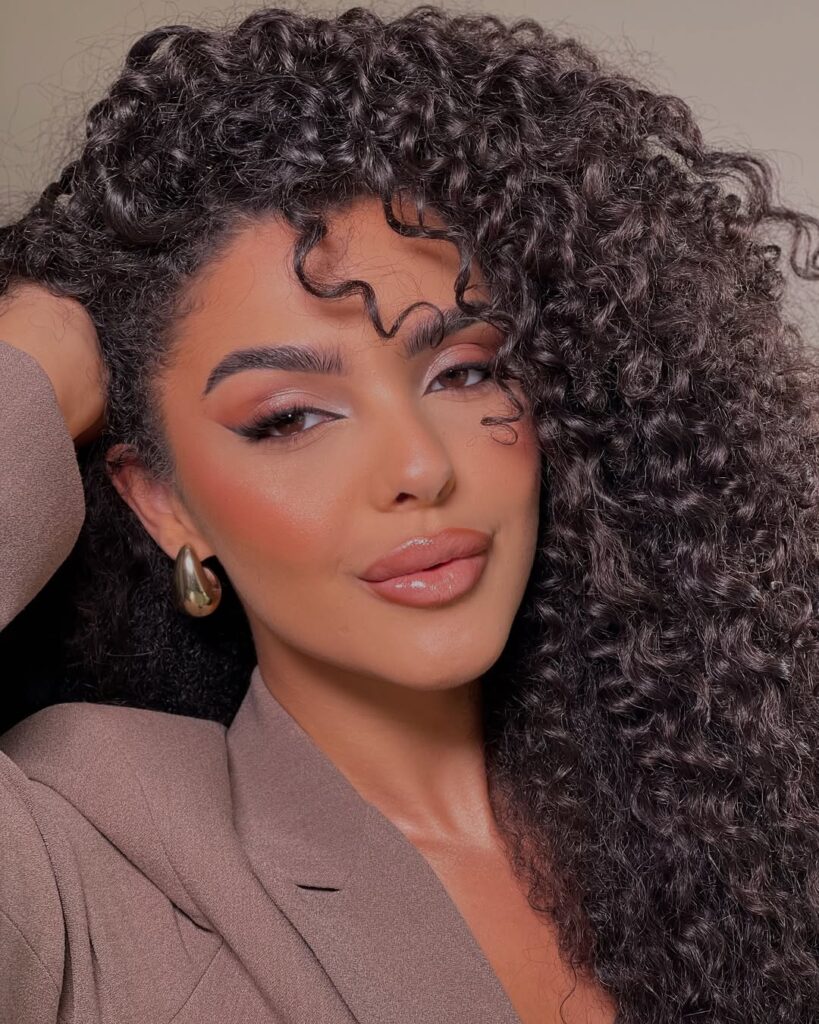 Mulher de pele preta, com cabelo cacheado escuro e maquiagem com delineado esfumado 