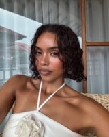Mulher de pele preta, com vestido branco e cabelo curto cacheado