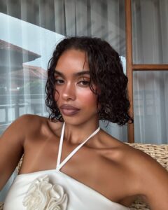 Mulher de pele preta, com vestido branco e cabelo curto cacheado