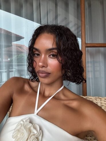 Mulher de pele preta, com vestido branco e cabelo curto cacheado