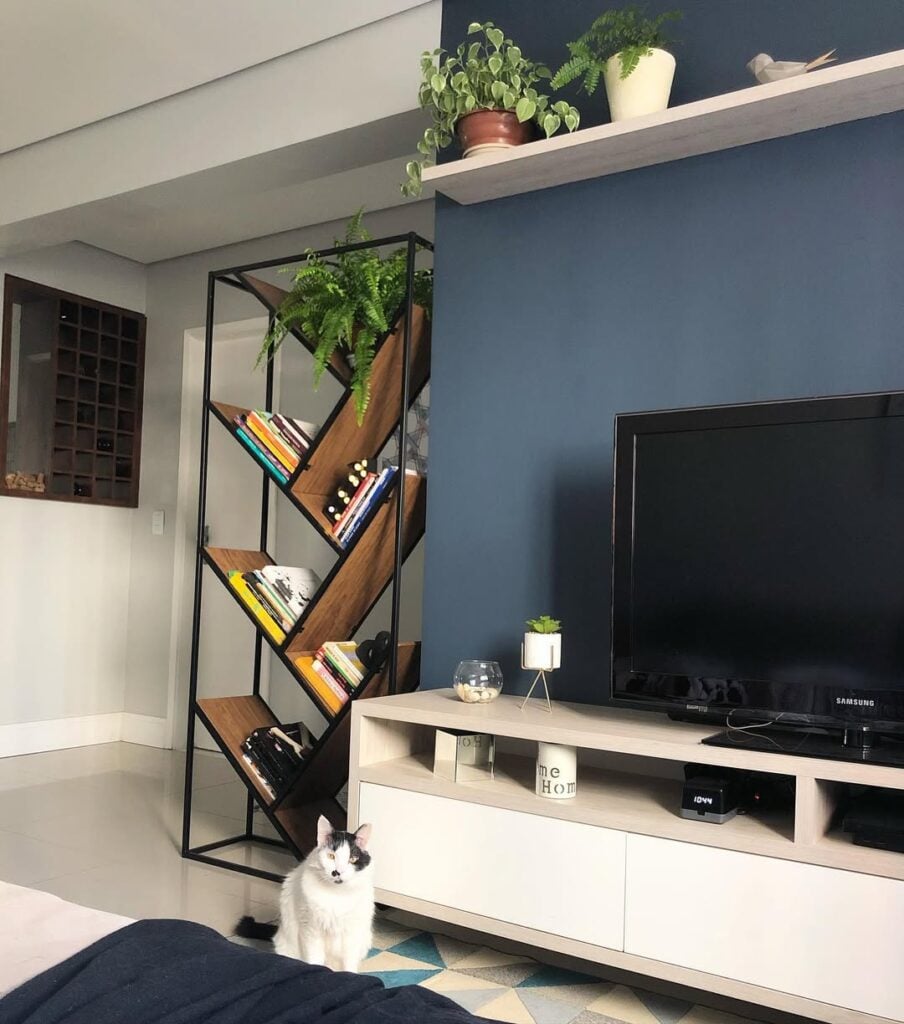 Sala com parede azul atrás da TV e estante com design diferente