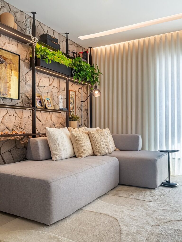 Sala de estar com sofá cinza, almofadas e estante de metal atrás