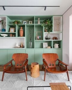 Sala de estar com poltronas em madeira e estante verde com nichos brancos