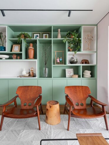 Sala de estar com poltronas em madeira e estante verde com nichos brancos