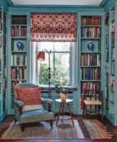 Ambiente com estantes de madeira azul com livros, poltrona e luminária de piso