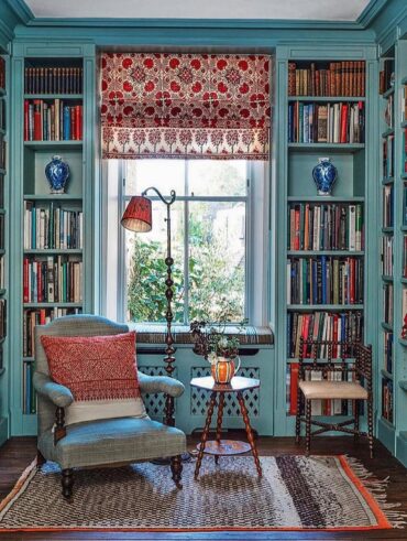 Ambiente com estantes de madeira azul com livros, poltrona e luminária de piso