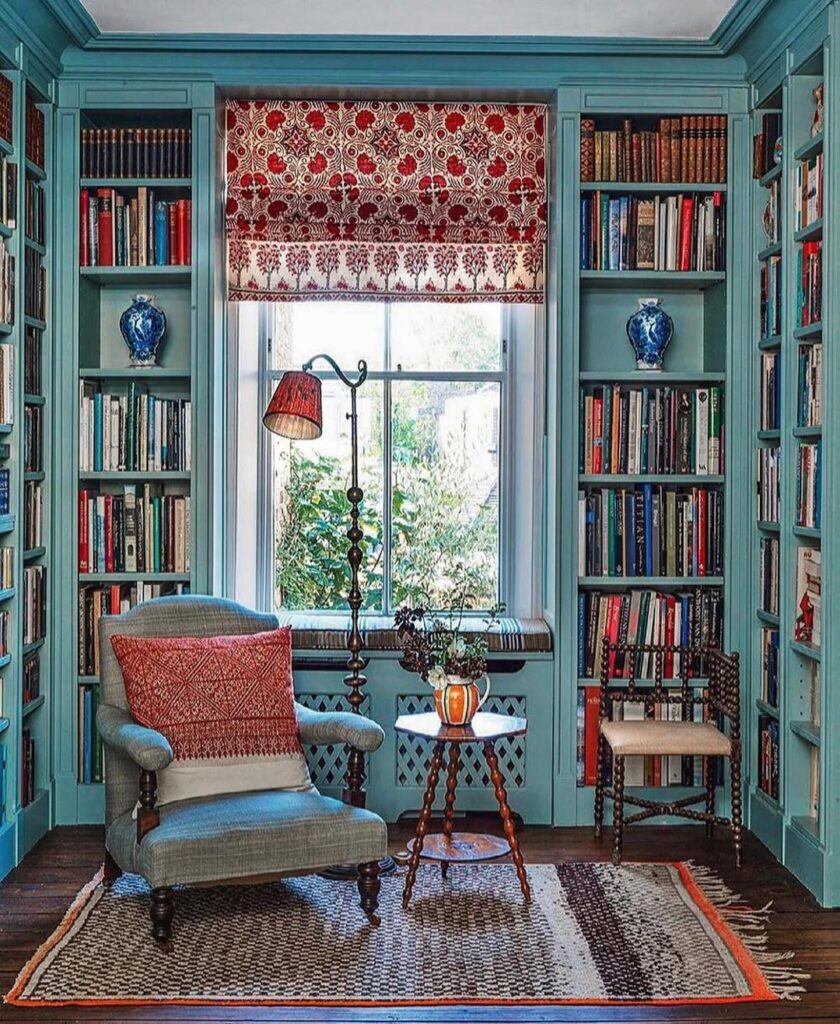 Ambiente com estantes de madeira azul com livros, poltrona e luminária de piso