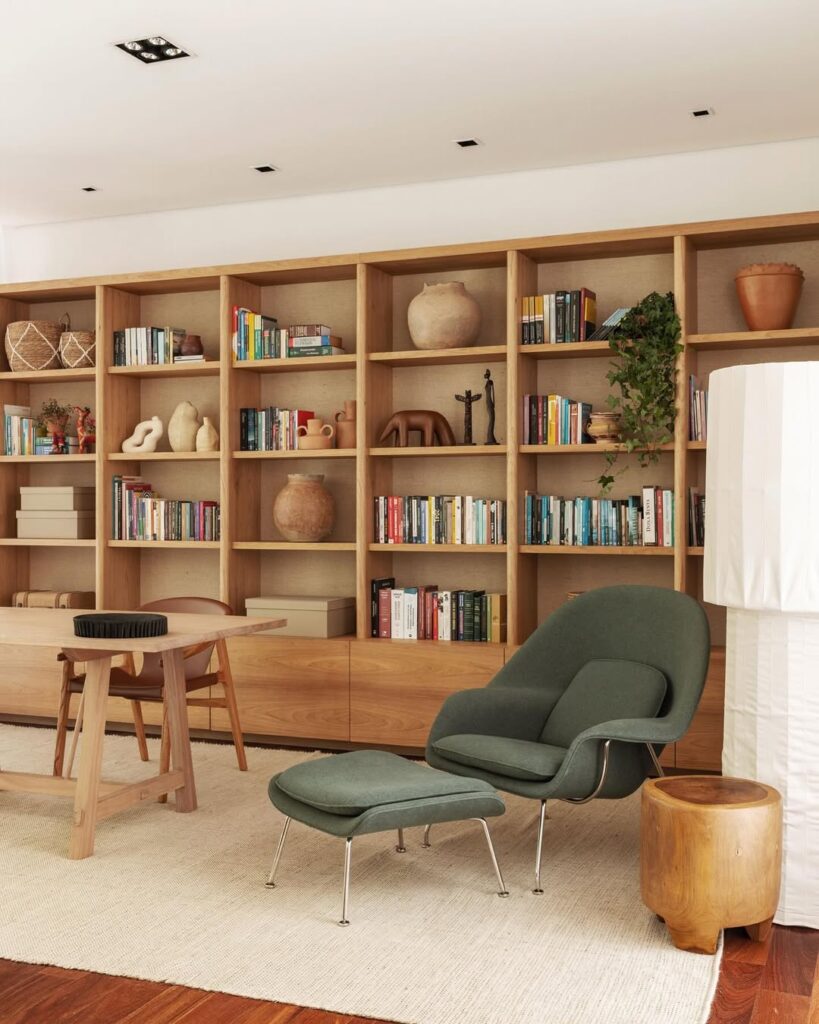Estante de madeira ampla com livros e objetos decorativos, e poltrona em tom de verde
