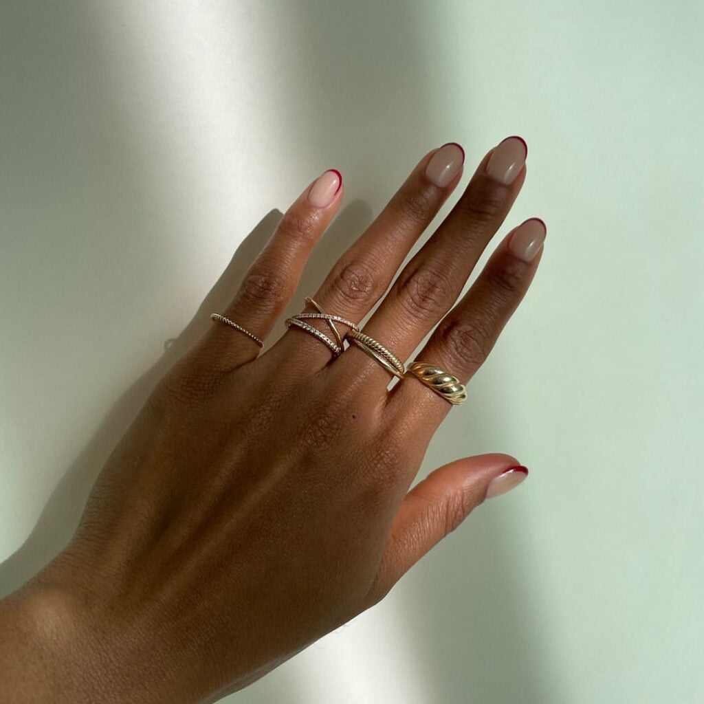 Mão de pele "média", com anéis em dourado e unha redonda neutra com francesinha burgundy