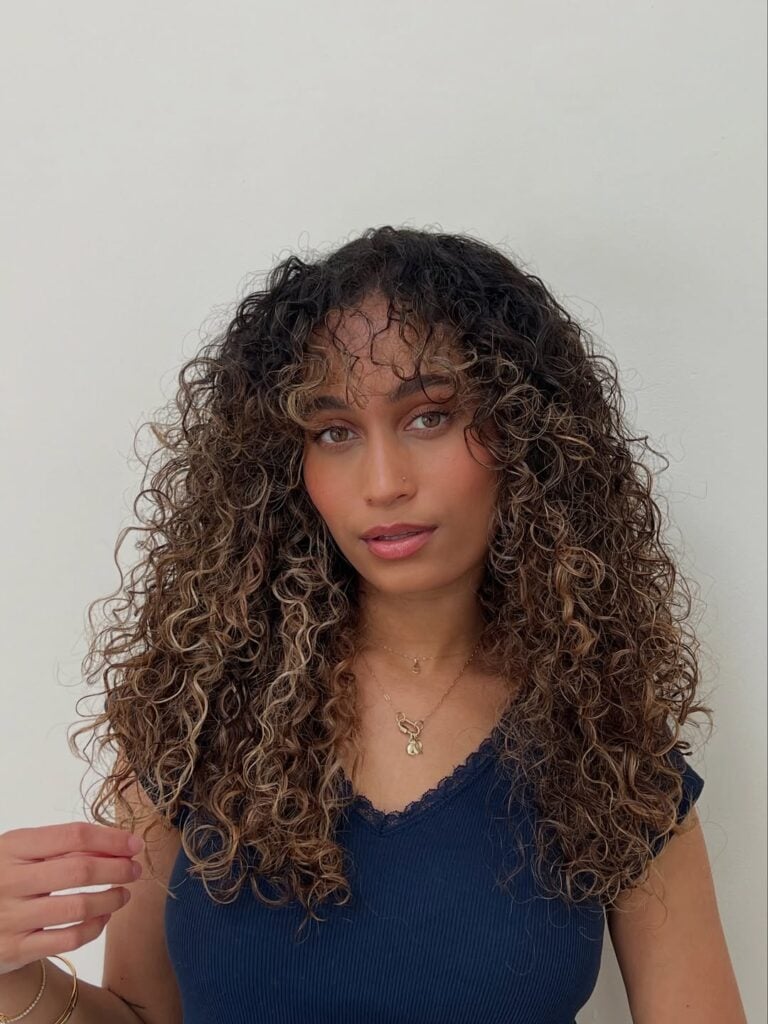 Mulher de pele "média", com blusa preta e cabelo cacheado com franja