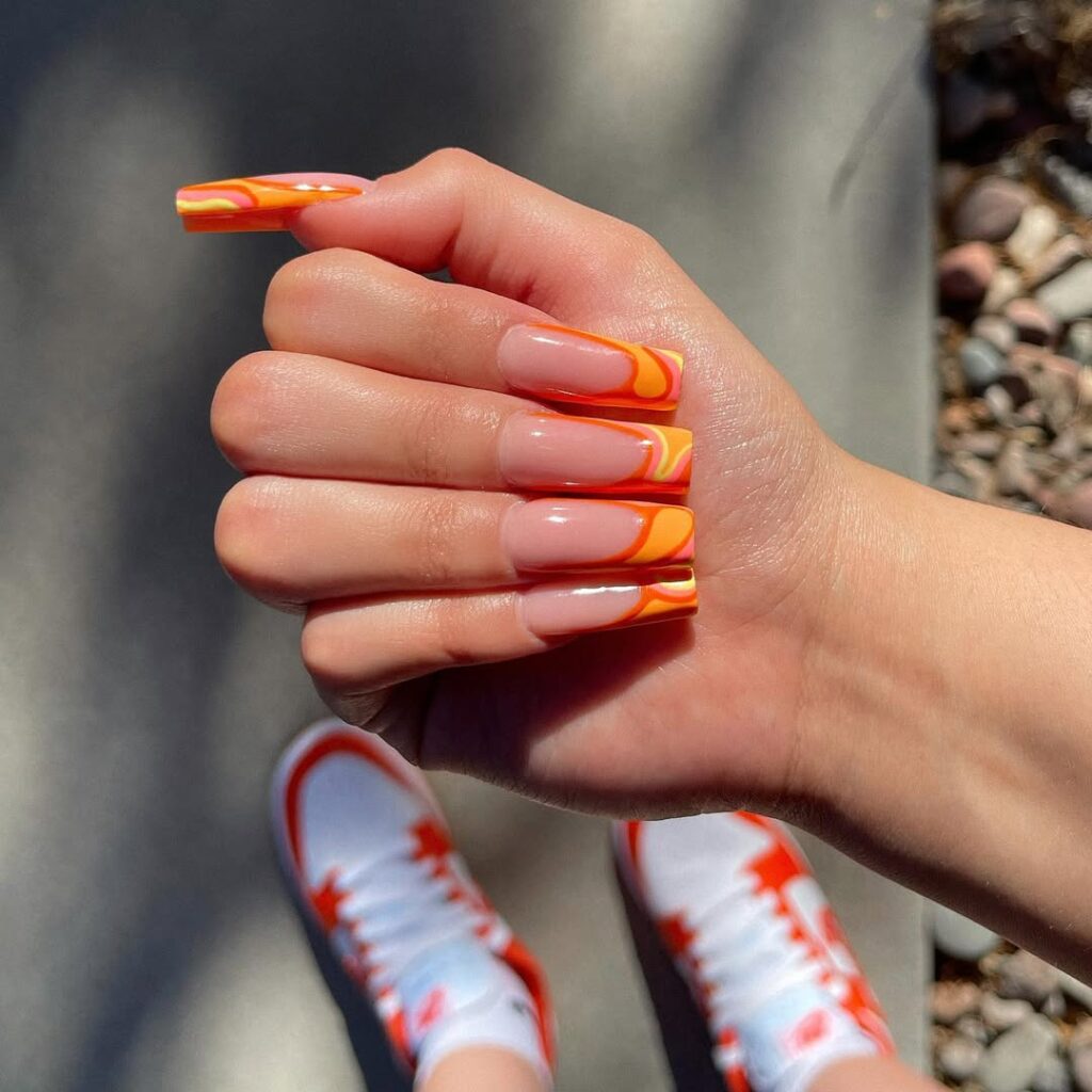 Mão de pele clara, com unha quadrada com inglesinha laranja decorada