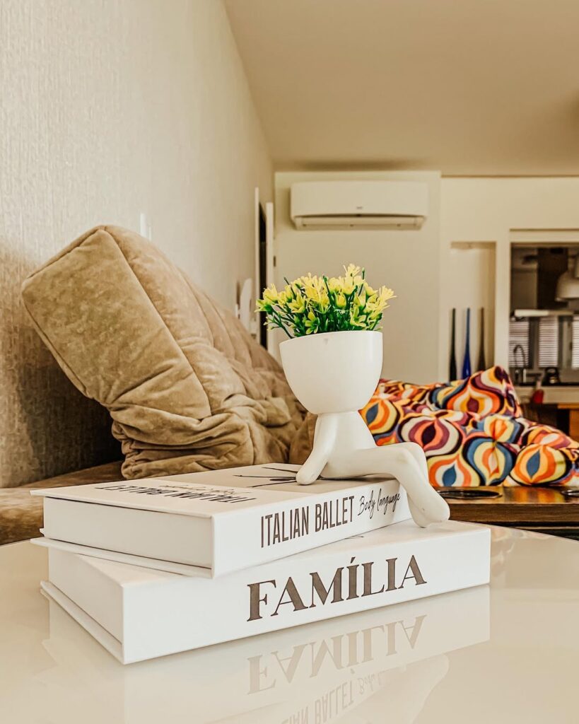 Mesa com caixas brancas de livros decorativos com um vainho de flores