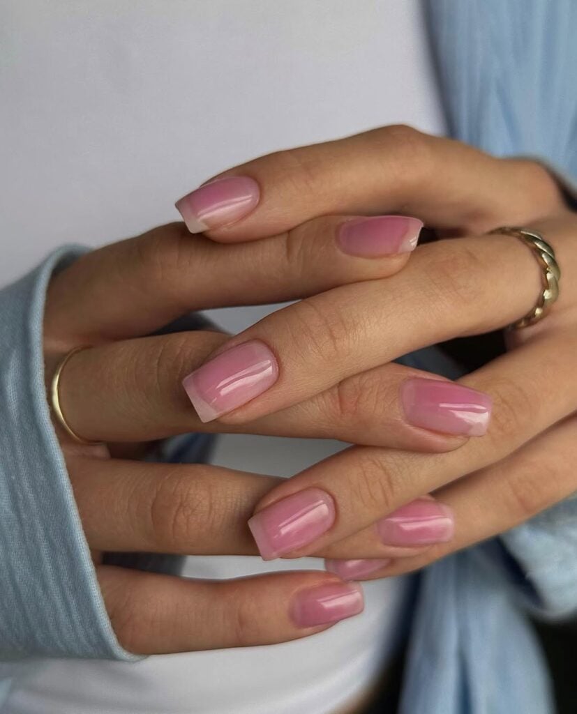 Mãos de pele clara, com anéis em dourado e unha quadrada rosa-translúcido 