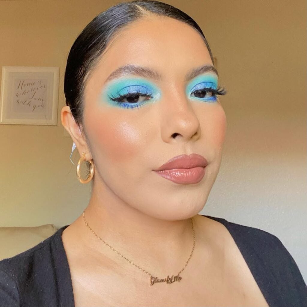 Mulher de pele clara, com acessórios em dourado e maquiagem com sombra azul 