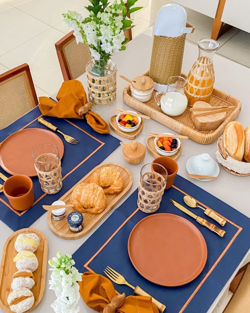 Mesa posta com jogo americano azul, canecas e pratos de cerâmica marrom