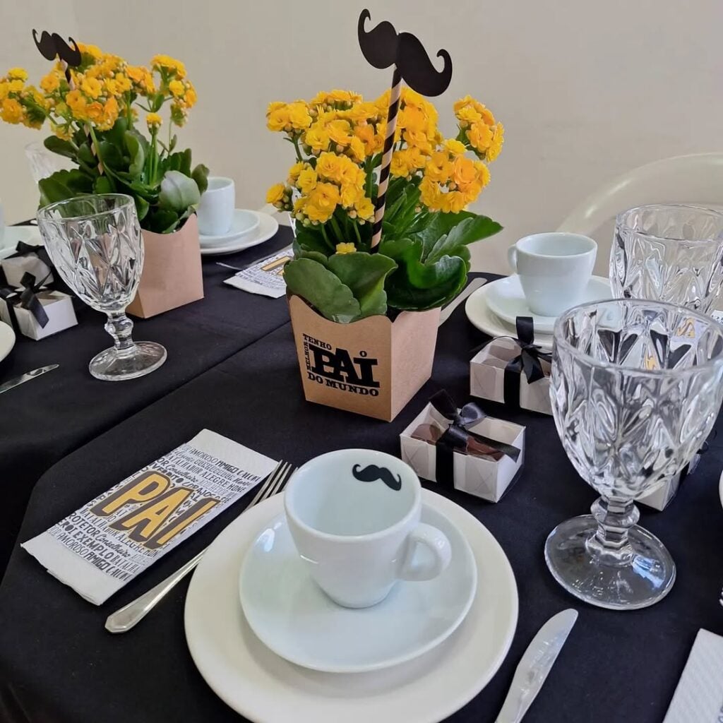 Mesa posta com toalha preta, louças brancas e flores amarelas