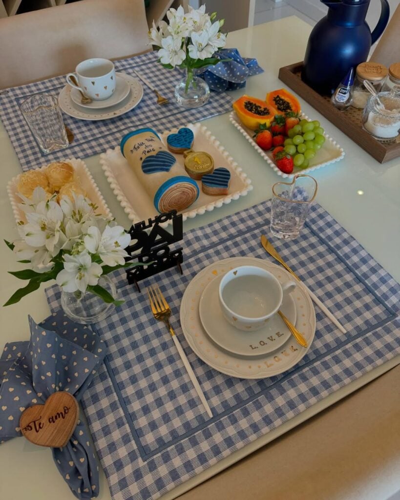 Mesa posta de Dia dos Pais com jogo americano em xadrez azul e branco, louças brancas e guardanapos azuis com corações brancos