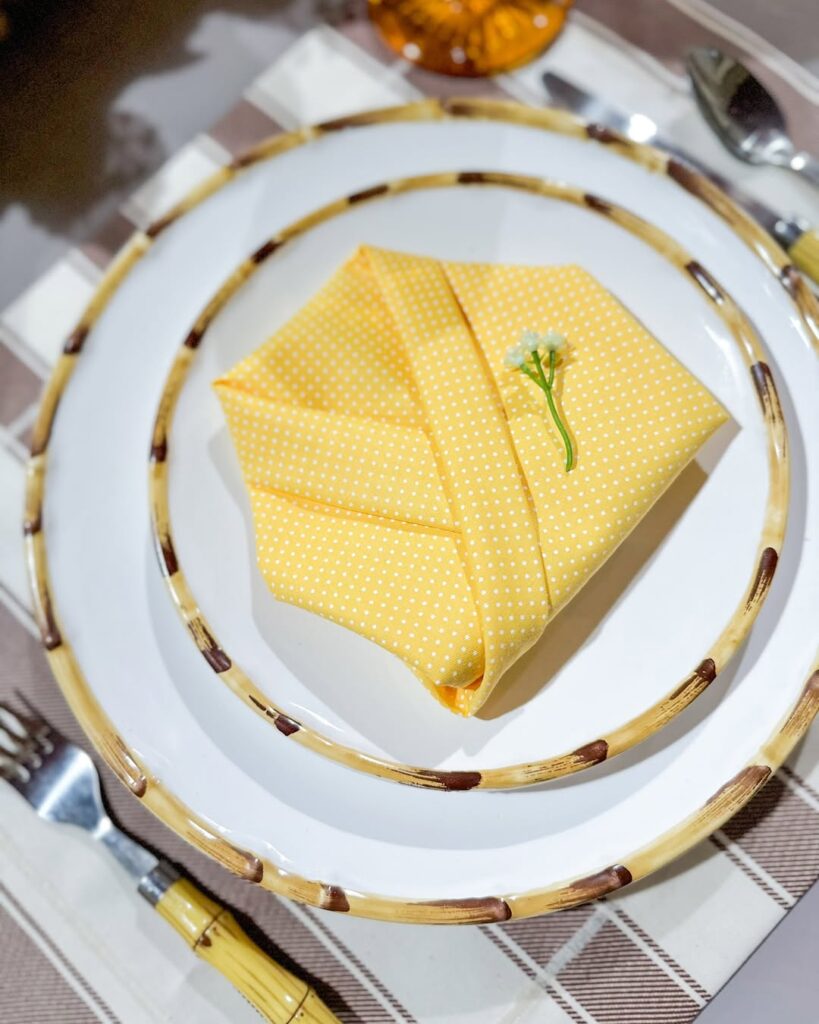 Mesa posta com pratos brancos com guardanapo amarelo dobrado em formato de camisa