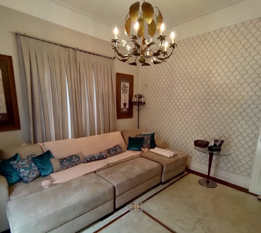 Sala com sofá grande, cortina e papel de parede neutro