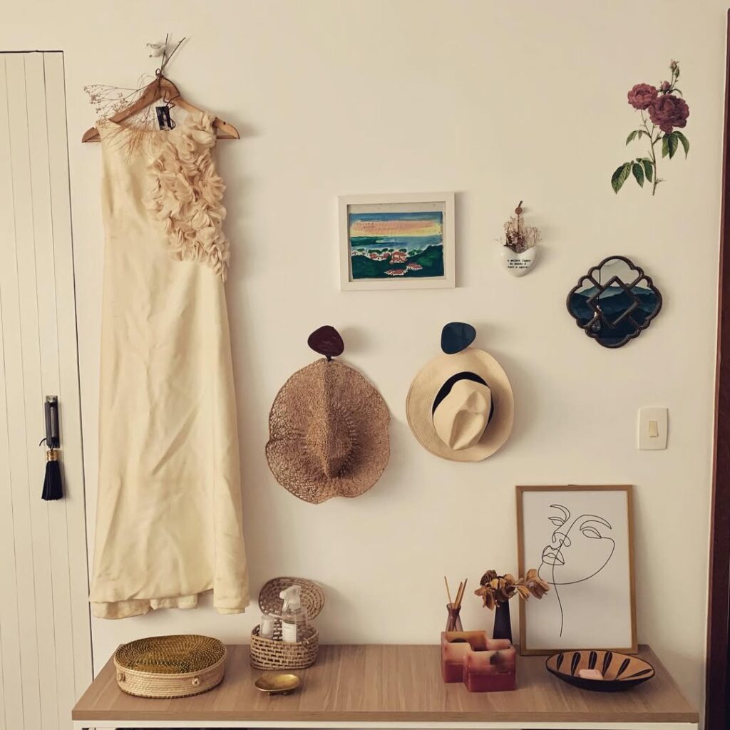 Parede branca com chapéus, quadro e vestido pendurado