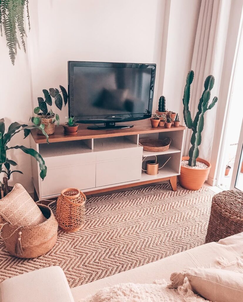 Sala de estar com rack branco, cestos de fibras naturais e vasos com cactos