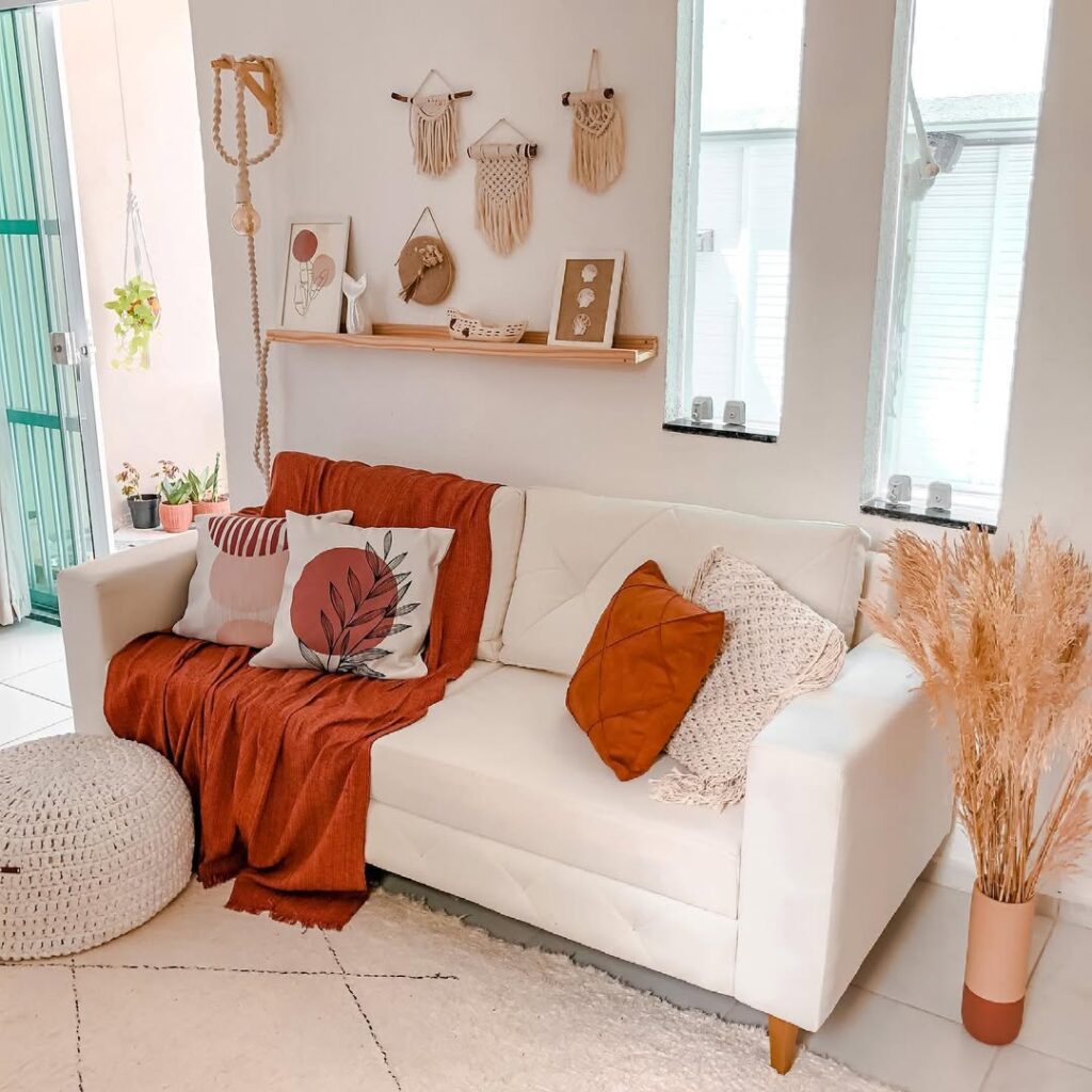 Sala no estilo boho com sofá branco, manta e almofadas terracota, pequenos macramês na parede