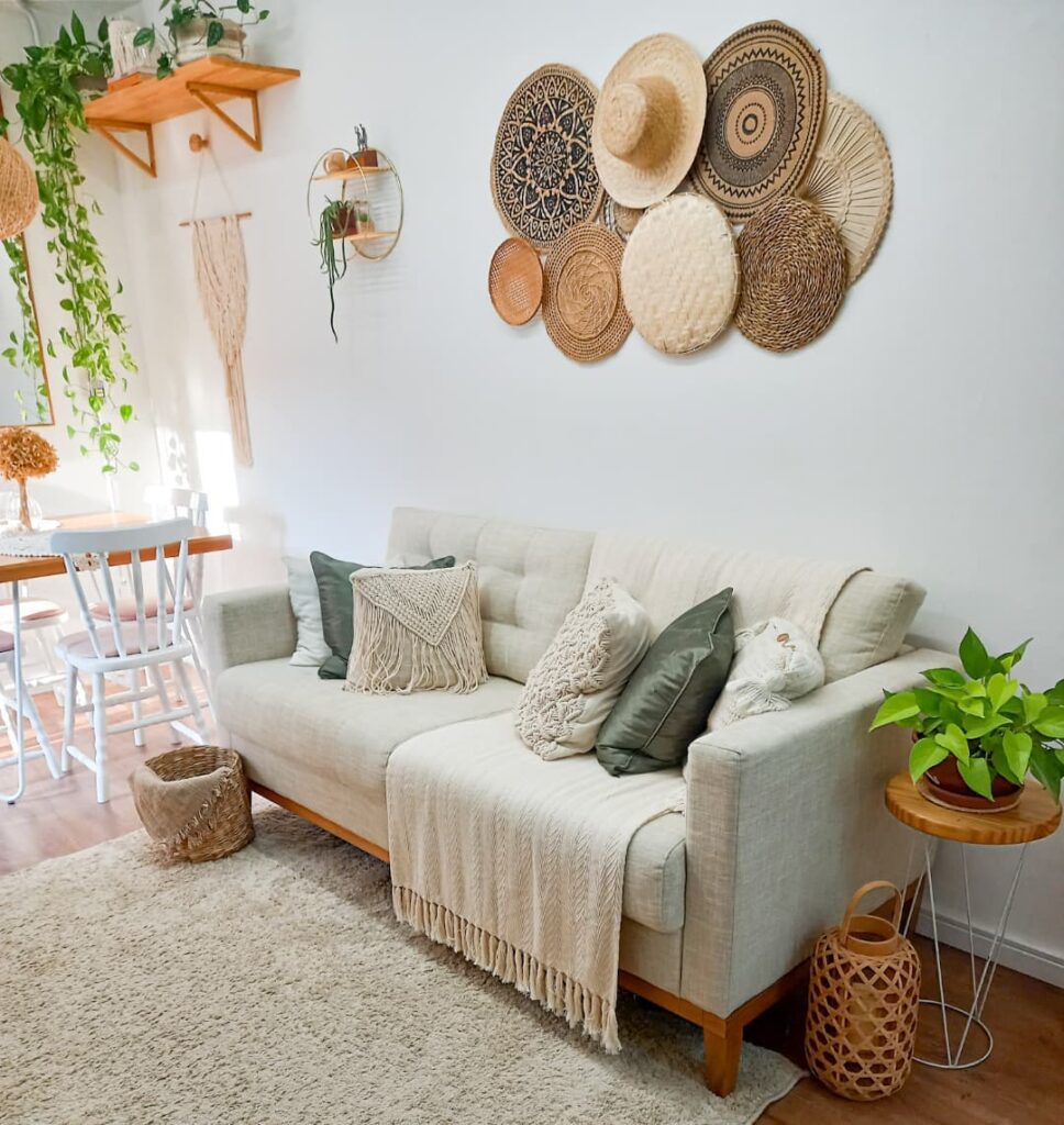 Sala com sofá cinza, manta e almofadas, e painel com itens de palha na parede