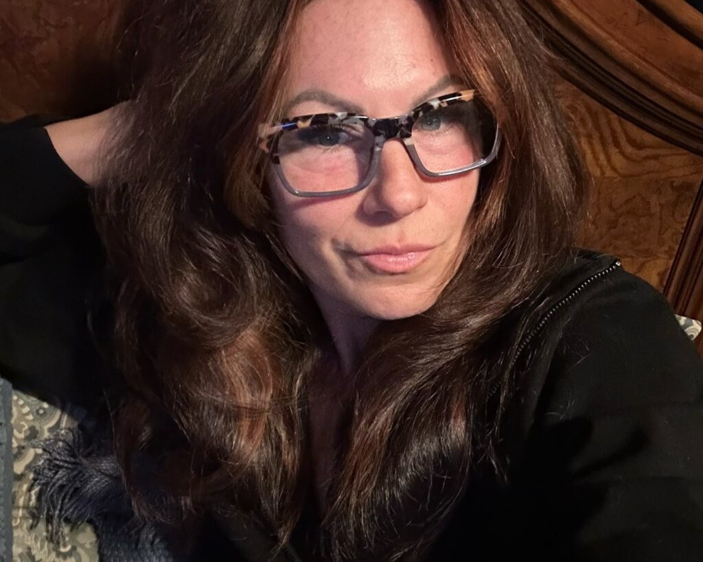 Mulher de 50 anos com pele madura, cabelo longo castanho e óculos de grau