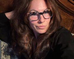 Mulher de 50 anos com pele madura, cabelo longo castanho e óculos de grau