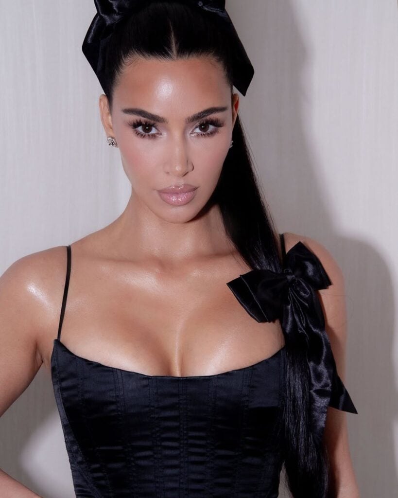 Kim Kardashian com vestido preto, cabelo escuro com laços e maquiagem clean 