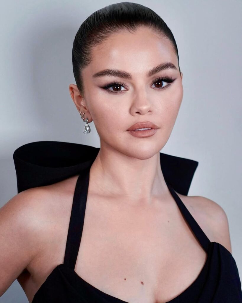 Selena Gomez com vestido preto, cabelo preso e maquiagem clean 