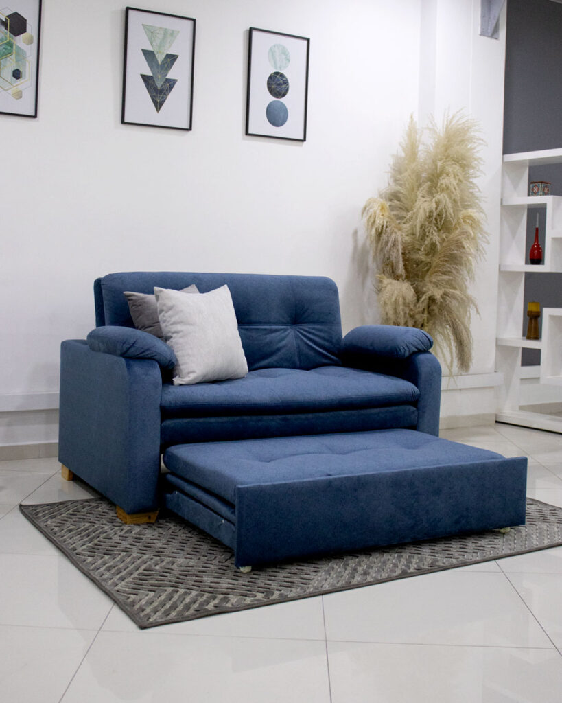 Sala com parede branca e quadros, sofá-cama em veludo azul e almofadas claras
