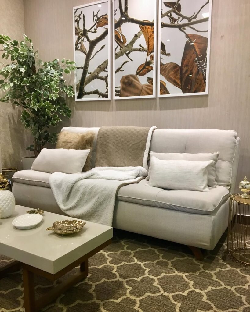 Sofá-cama bege em sala com tapete, quadros e vaso com plantas